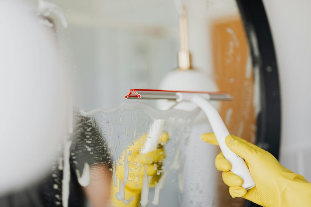 pexels photo 4239145 4239145 Person using a squeegee to clean a foamy bathroom mirror indoors.