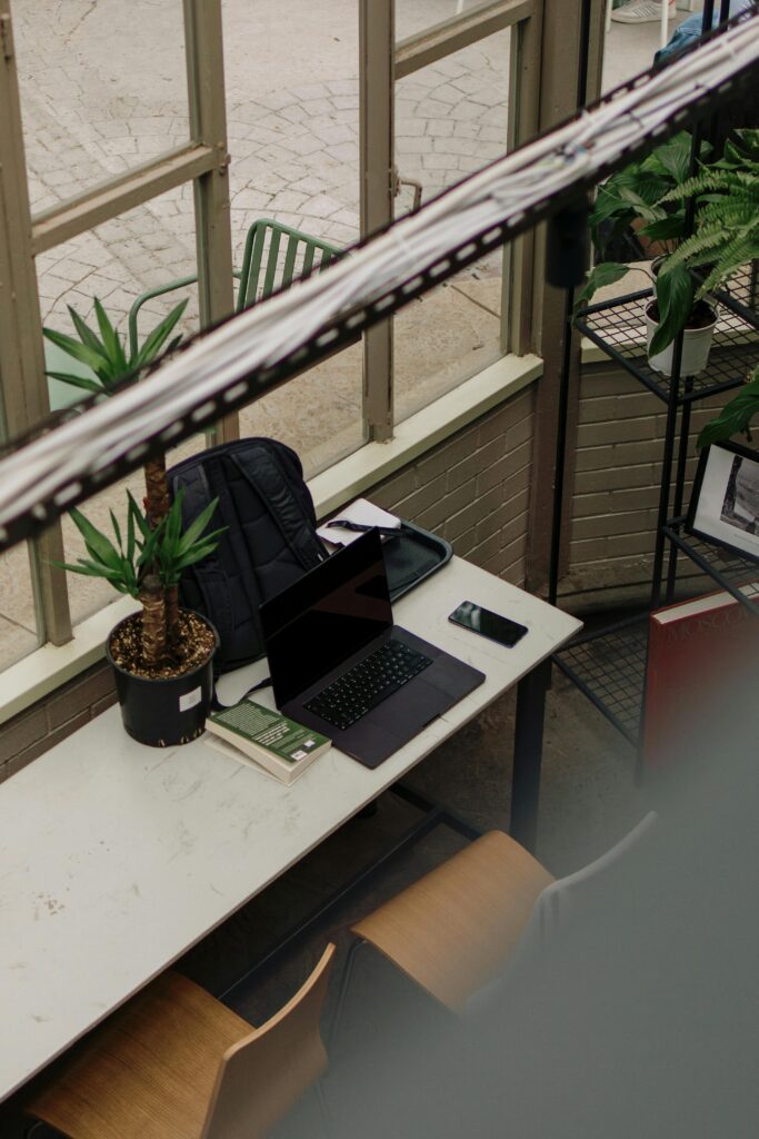 A cozy indoor workspace featuring a laptop, smartphone, and potted plants, creating a productive environment.
